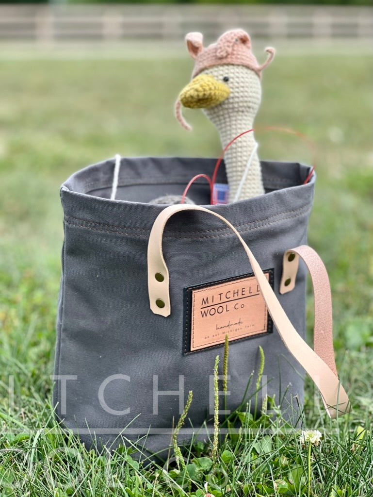 An adorable crocheted Amigurumi Goose sits inside our grey twill simple tote in a sunny pasture