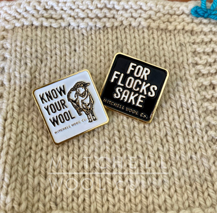 A black For Flocks Sake pin sits to the right of a white Know Your Wool pin on a natural cormo worsted wool swatch.
