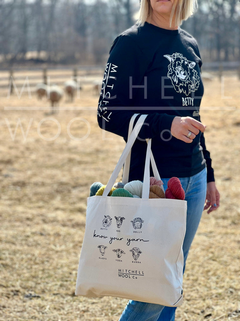Sherry stands in the pasture wearing a Woah Big Betty black tee and holding our Made in the USA cotton stash bag with our own sheep on it. It easily fits a dozen skeins of yarn or more.
