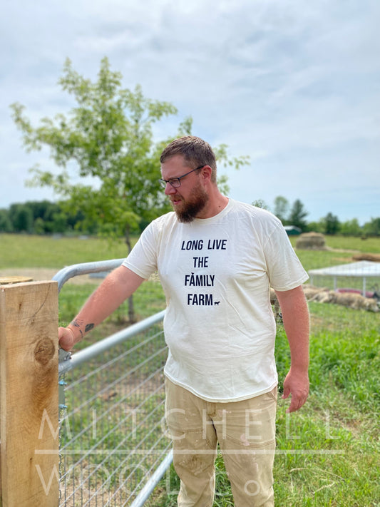 Luke opens the gate to rotate our flock into a fresh new pasture. He is wearing an organic natural colored cotton tee shirt that says "Long Live the Family Farm" in black ink. The shirt was made in the USA 