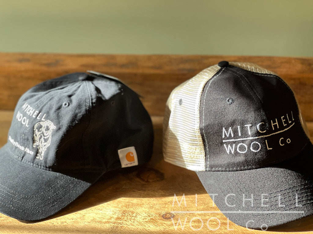 The MWC black cotton Carhartt and MWC black/natural trucker hat sit in the warm afternoon sun upon a worn pine table.