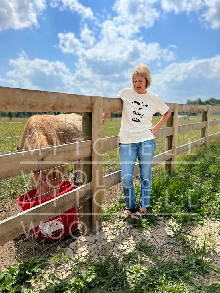 Sherry stands in a dry pasture with cracked soil, we need rain badly. Such is the life of a farmer, living for the weather. She wears our organic cotton made in the USA tee shirt with the words Long Live the Family Farm in black ink and animals in silhouette.