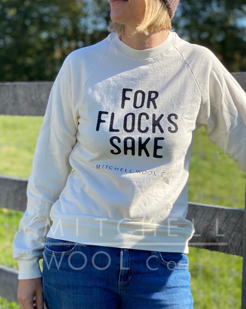 Sherry stands next to her black three board fence wearing a natural organic cotton For Flocks Sake sweatshirt in size XS.