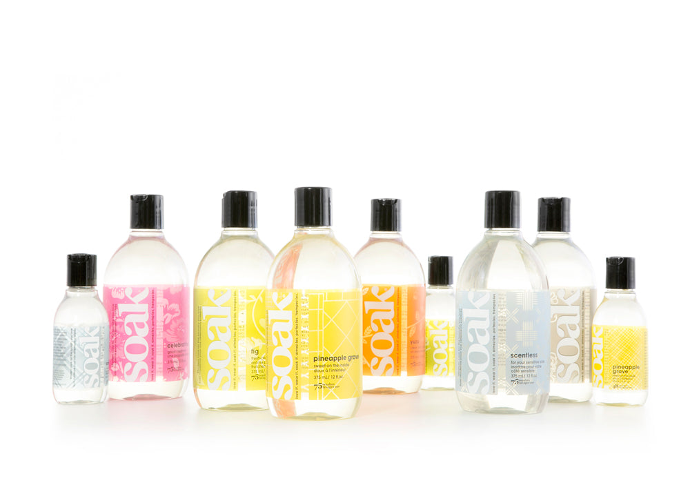 The entire scent collection of Soak Wash in size 12 oz and 3 oz bottles sit on a white field