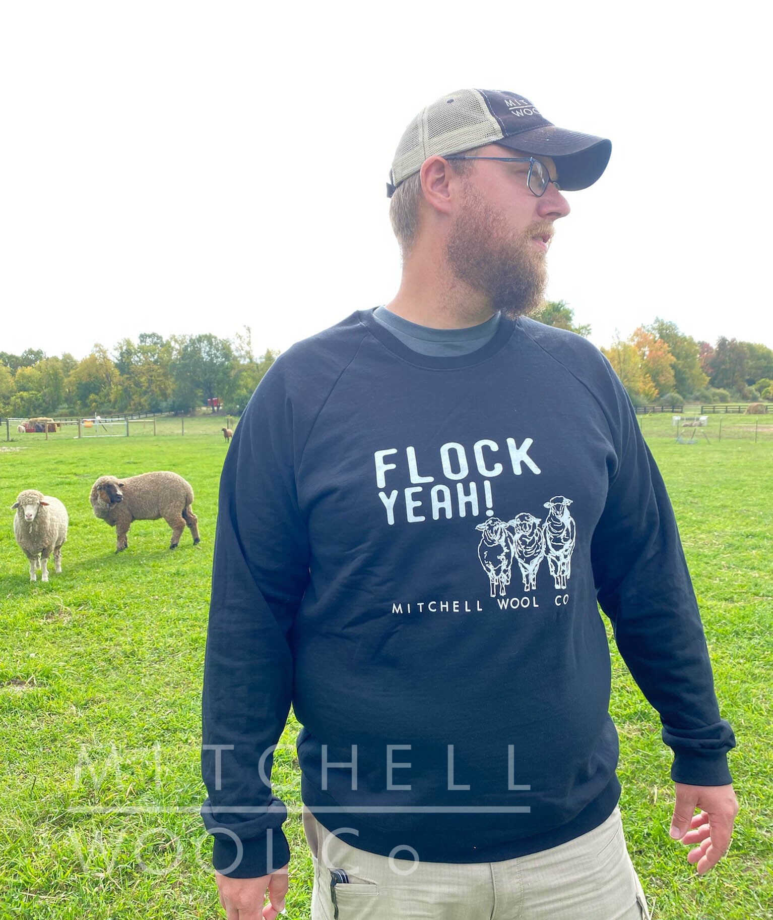 Luke stands in the pasture with Chester and Charlotte wearing a black organic cotton sweatshirt and a MWC trucker hat. 