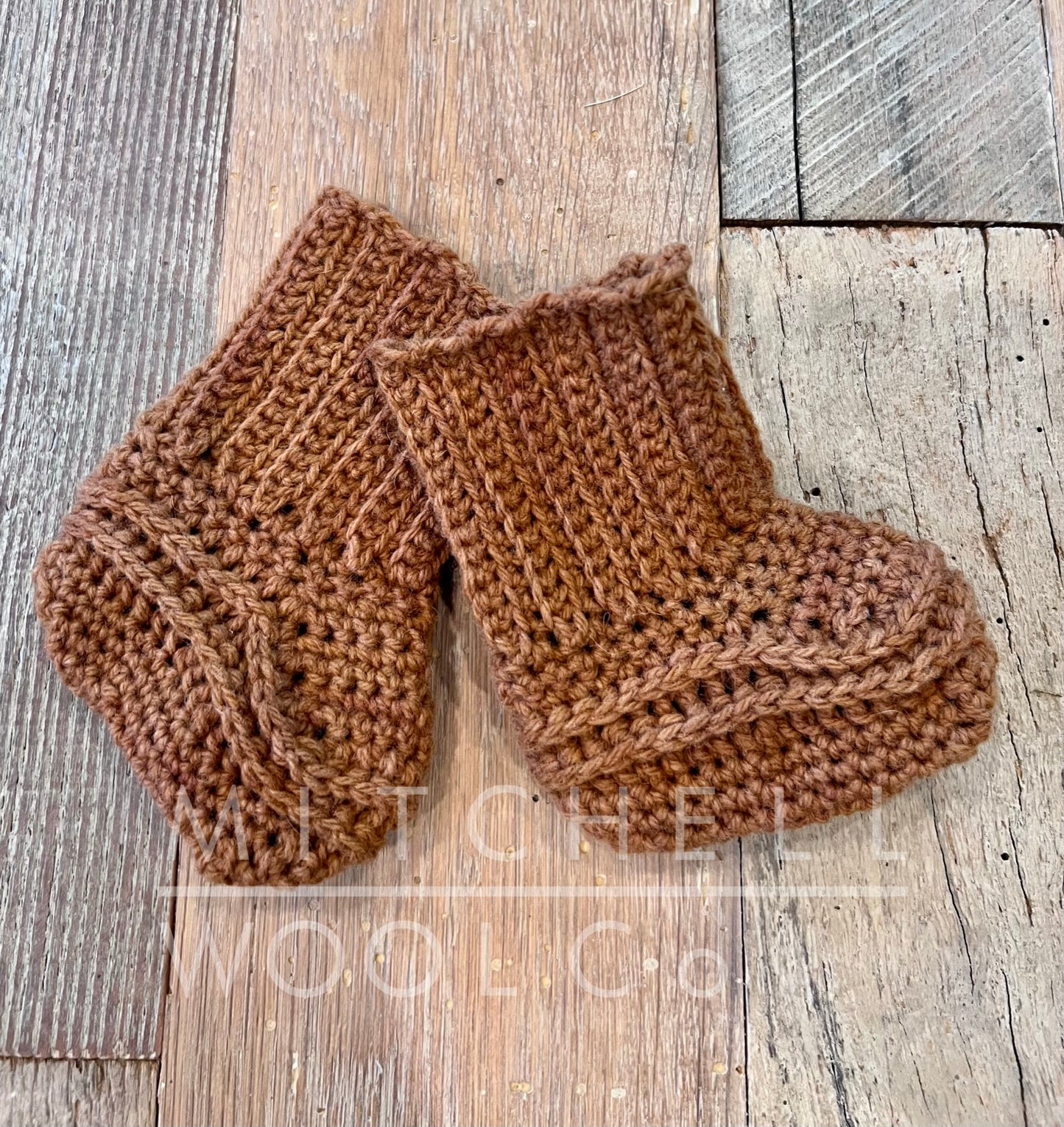 Hand crocheted booties dyed with cutch cormo dk yarn sit on our worn barn wood shop floor.