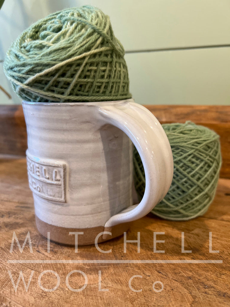 Look at that PERFECT handle! MWC white mug sits on our old wood sideboard with caked balls of our new Mackinac Bridge botanical dyed yarn