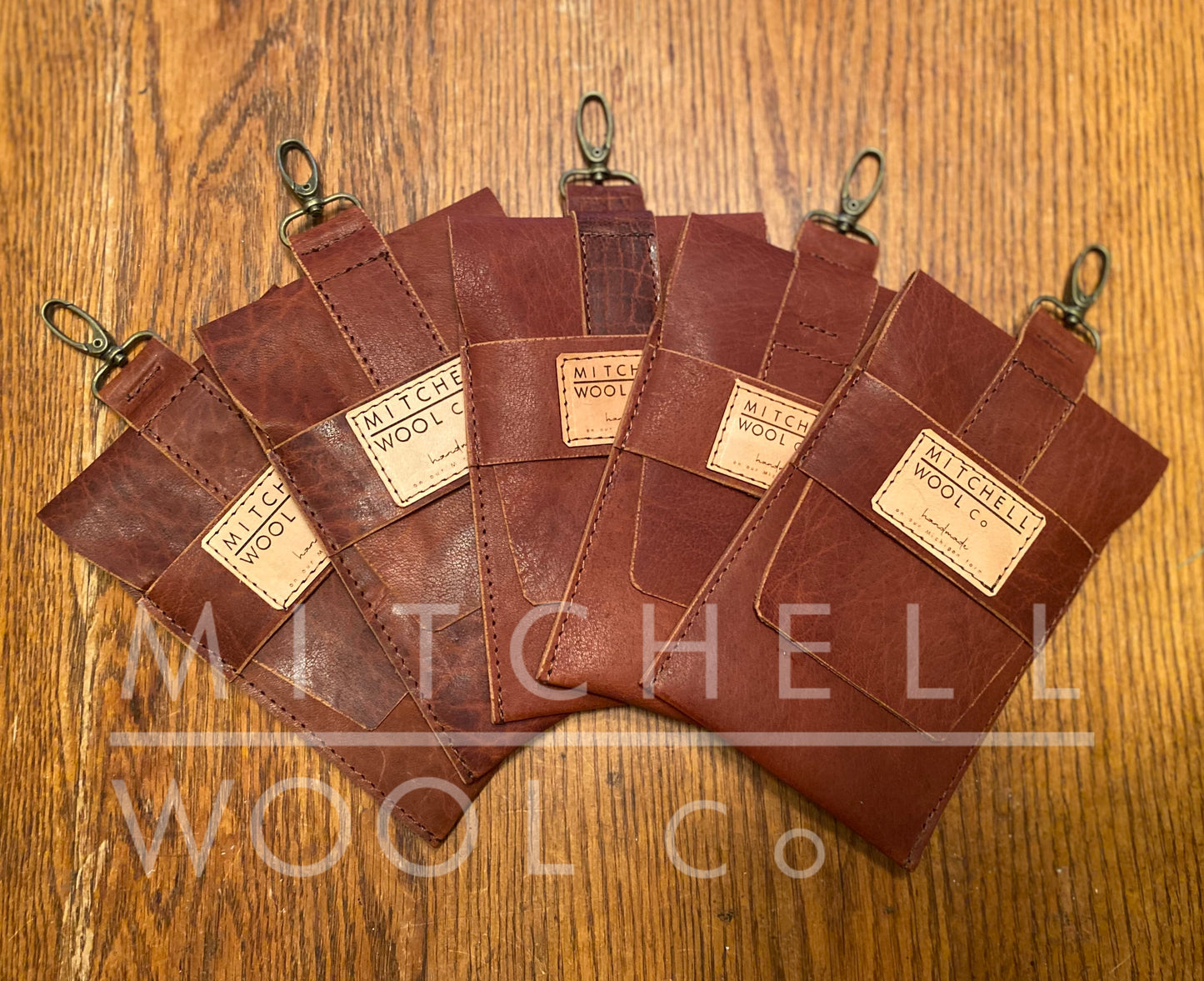 five hand made leather cell phone pouches sit on an oak table